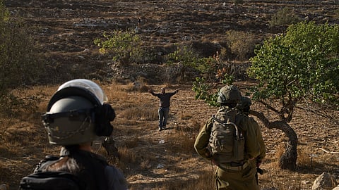 An Israeli settler gestures as Israeli soldiers block access for Palestinians to an area for harvesting olives in the West Bank village of Sa'ir, near Hebron, Thursday, Oct. 23, 2025.