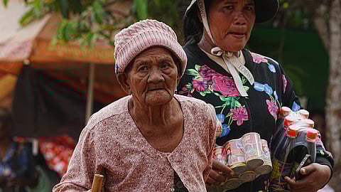 A woman, left, walks as she takes refuge at Batthkoa Primary School in Oddar Meanchey province, Cambodia, Wednesday, Dec. 10, 2025, after fleeing from home following fighting between Thailand and Cambodia over territorial claims.