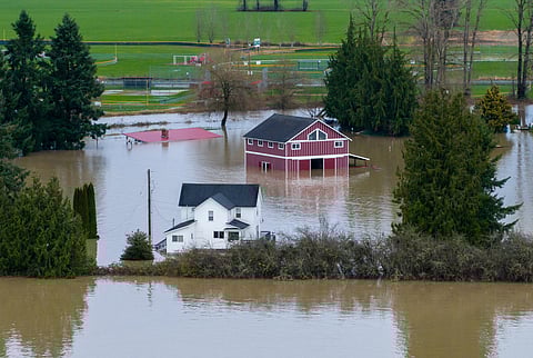 An aerial view of a home and a barn surrounded by floodwaters in Snohomish, Wash., Thursday, Dec. 11, 2025.