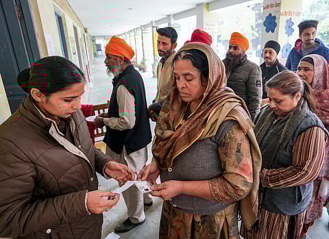 A police official checks documents of voters at a polling station during 'Zila Parishad' and 'Panchayat Samiti' elections, on the outskirts of Amritsar, Punjab, Sunday, Dec. 14, 2025.