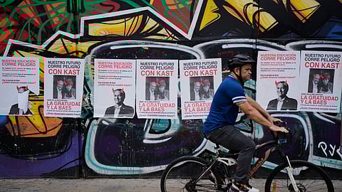 A man cycles past campaign ads for presidential candidate Jose Antonio Kast, reading in Spanish, "Our future is in danger," ahead of the presidential runoff election in Santiago, Chile, Friday, Dec. 12, 2025.