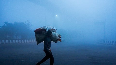 A man carrying sacks of goods walks by amid dense fog on a winter morning, at Mayur Vihar area, in New Delhi, Saturday, Dec. 20, 2025.