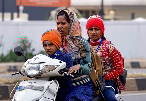 A woman rides a scooter with her children, all dressed in woollens, in Chikkamagaluru on Monday. Several parts of the state is in the grip of a cold wave