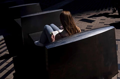 A woman reads a book in the afternoon sun on a bench outside South Station in Boston, on Friday, May 31, 2024.
