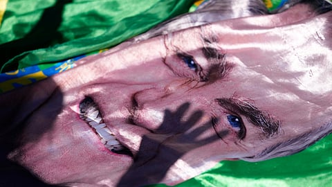 The shadow of a supporter of former President Jair Bolsonaro is cast on an image of him displayed outside the hospital where he was transported from prison for surgery the next day, in Brasilia, Brazil, Wednesday, Dec. 24, 2025.