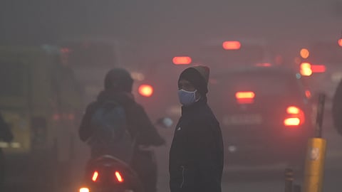 People walk along a road amid dense fog, affecting visibility on a winter morning, in New Delhi on Monday.