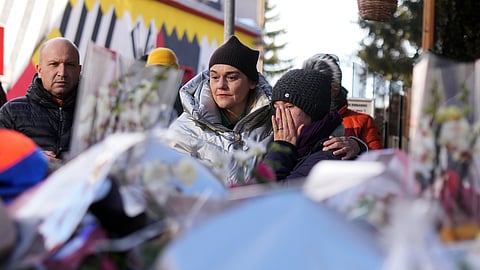 People mourn behind flowers and letters near the sealed off Le Constellation bar, where a devastating fire left dead and injured during the New Year's celebrations in Crans-Montana, Swiss Alps, Switzerland, Friday, Jan. 2, 2026.