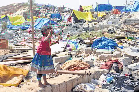 A girl drinks water amid the rubble of her home following the demolition drive, in Kogilu on Monday
