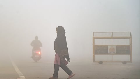 A woman crosses a road amid dense fog on a winter morning, in Prayagraj.