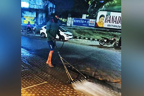 A BMC sanitation worker spraying the modified pressure jet on a pavement in the city