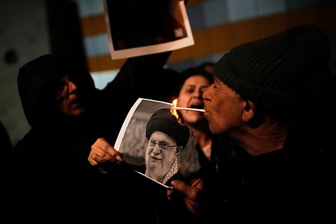 A demonstrator lights a cigarette with a burning poster depicting Supreme Leader Ayatollah Ali Khamenei during a rally in support of Iran's anti-government protests, in Holon, Israel Wednesday, Jan. 14, 2026.