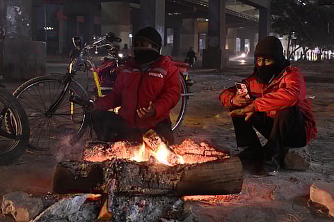 People sit around a bonfire to warm themselves on a cold winter Evening in New Delhi on January 16, 2026.