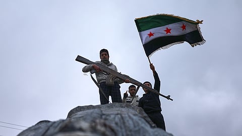 Residents wave a Syrian flag atop a toppled statue of a female Kurdish fighter, with one holding the statue's replica AK-47 that was part of the statue, after the takeover of the town by Syrian government forces from US-backed Syrian Democratic Forces (SDF), in Tabqa, eastern Syria, Sunday, Jan. 18, 2026.