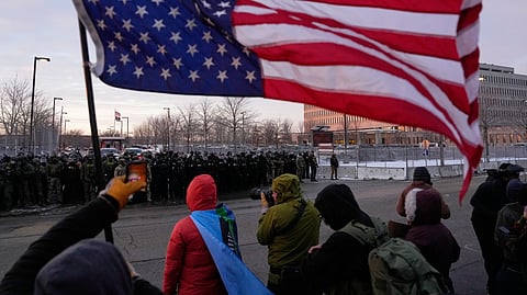 A person holds an upside-down American flag as law enforcement stand during a protest outside the Bishop Henry Whipple Federal Building on Saturday, Jan. 17, 2026, in Minneapolis.