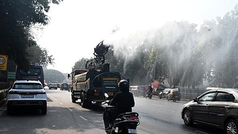 Commuters ride past an anti-smog gun spraying water to curb air pollution amid heavy smog conditions in New Delhi.