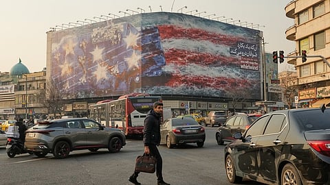 A man walks among vehicles in front of a billboard depicting a damaged US aircraft carrier with disabled fighter jets on its deck and a sign reading in Farsi and English, "If you sow the wind, you'll reap the whirlwind," at Enqelab-e-Eslami (Islamic Revolution) Square in Tehran, Iran, Sunday, Jan. 25, 2026.
