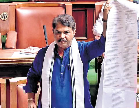 Opposition leader R Ashoka displays a list of 454 projects and schemes named after the Gandhis, in the Legislative Assembly in Bengaluru on Monday.