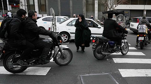 A woman crosses a square as motorbikes ride past in downtown Tehran, Iran, Tuesday, Feb. 24, 2026.