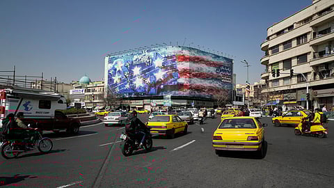 Vehicles pass a billboard depicting a US aircraft carrier with damaged fighter jets on its deck and a sign in Farsi and English reading, "If you sow the wind, you'll reap the whirlwind," at Enqelab-e-Eslami (Islamic Revolution) Square in Tehran, Iran, Sunday, Feb. 22, 2026.