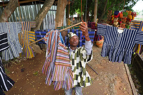 Clement Azaabire hangs traditional fugu garments under a tree on display for sale along a street in Accra, Ghana.