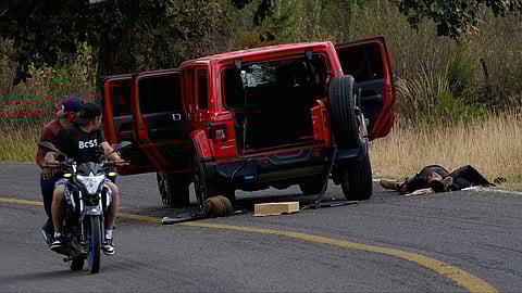 People drive past a body lying beside a bullet-riddled vehicle in Tapalpa, Mexico, Monday, Feb. 23, 2026, a day after the Mexican army killed Jalisco New Generation Cartel leader Nemesio Oseguera Cervantes, known as "El Mencho."