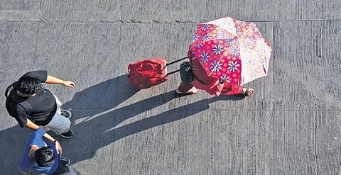 A passenger at Bengaluru’s Kempegowda Bus Terminal uses an umbrella to protect herself from the summer heat on Thursday
