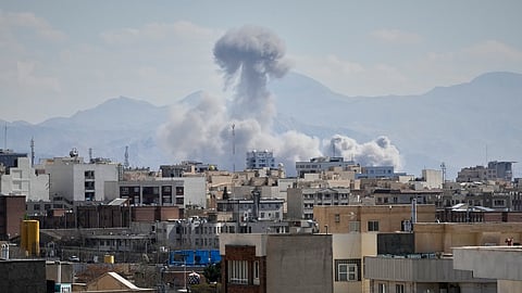 People watch from a rooftop as a plume of smoke rises after a strike in Tehran, Iran, Sunday, March 1, 2026.