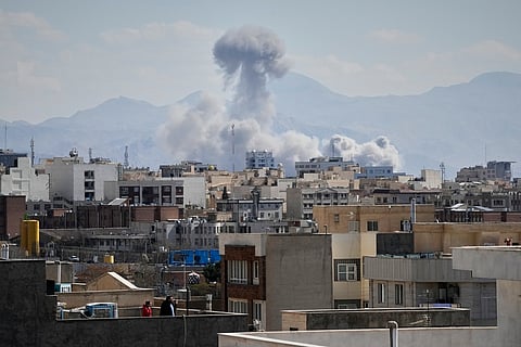 People watch from a rooftop as a plume of smoke rises after a strike in Tehran, Iran, Sunday, March 1, 2026.