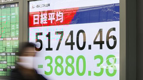 People walk in front of an electronic stock board showing Japan's Nikkei index at a securities firm Monday, March 9, 2026, in Tokyo.