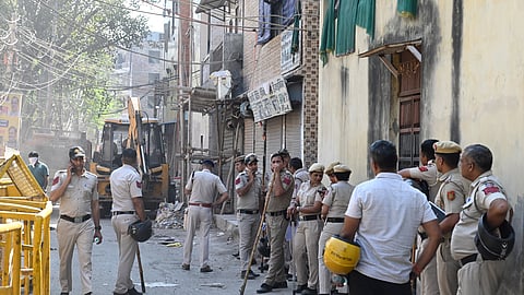 Security personnel stand guard as Municipal Corporation of Delhi (MCD) carries out bulldozer action against the property of the accused in Holi clash case, at JJ colony, Uttam Nagar, in New Delhi on Sunday.