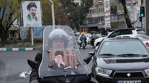 A man rides his motorcycle with a poster of the late Iranian Supreme Leader Ayatollah Ali Khamenei as a banner at the rear, showing a portrait of his son and successor, Ayatollah Mojtaba Khamenei, in downtown Tehran, Iran, Tuesday, March 10, 2026.