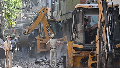 Security personnel stand guard as Municipal Corporation of Delhi (MCD) carries out bulldozer action against the property of the accused in Holi clash case, at JJ colony, Uttam Nagar, in New Delhi on Sunday.