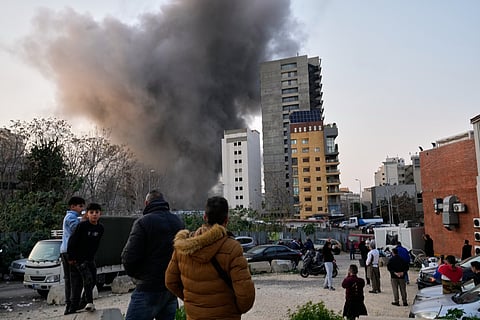 Residents watch as smoke rises from a nearby building during an Israeli strike in central Beirut, Lebanon, Thursday, March 12, 2026.