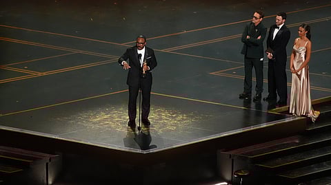 Ryan Coogler accepts the award for writing (original screenplay) for "Sinners" during the Oscars on Sunday, March 15, 2026, at the Dolby Theatre in Los Angeles. Robert Downey Jr., second right, and Chris Evans looks on from right.