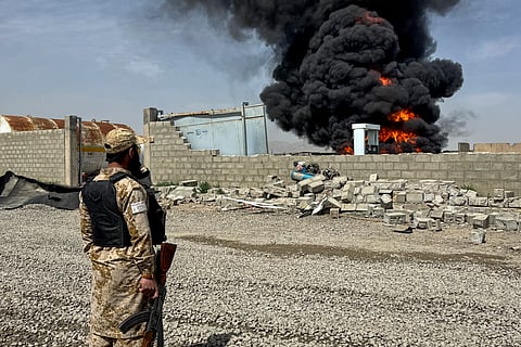 A Taliban security personnel stands as smoke rises from the site after overnight Pakistani airstrikes hit oil depots for commercial airlines, near the Kandahar airport in the Daman district of Kandahar province on March 13, 2026.