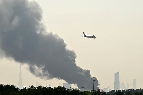 An Emirates aircraft flies past plumes of smoke from a fire near Dubai International Airport after a drone strike on March 16.