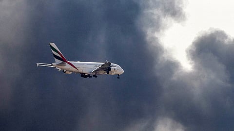 An Emirates Airbus A380 aircraft prepares for landing as a smoke plume rises from an ongoing fire near Dubai International Airport in Dubai on March 16, 2026.