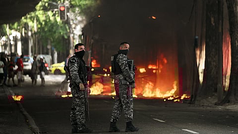 Police officers stand next to a bus set on fire allegedly by drug traffickers during a police operation in central Rio de Janeiro, Brazil, on March 18, 2026.