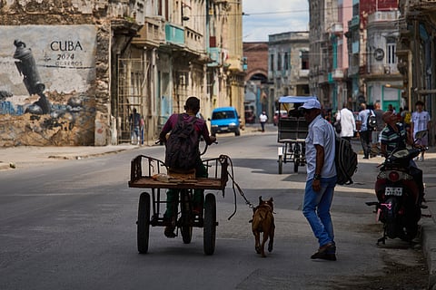 A man rides a tricycle with his leashed dog running alongside him during a blackout in Havana, Cuba, Monday, March 16, 2026.