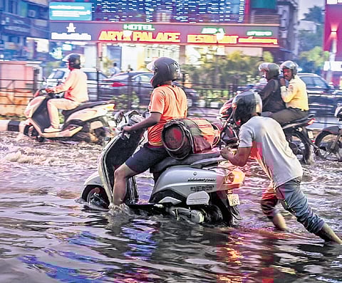 A man carries an LPG cylinder on his scooter while another pushes the vehicle after it breaks down in knee-deep water, at Janpath on Thursday