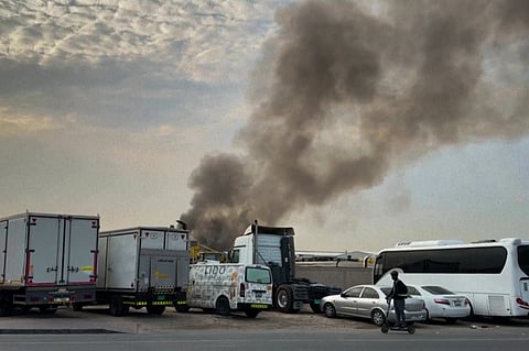 In this file image, used for representational purposes, shows a man riding past as smoke rises from a fire which, according to the authorities was caused by a successful interception, at Dubai's Al Quoz Industrial area, United Arab Emirates, on Friday, March 13, 2026.