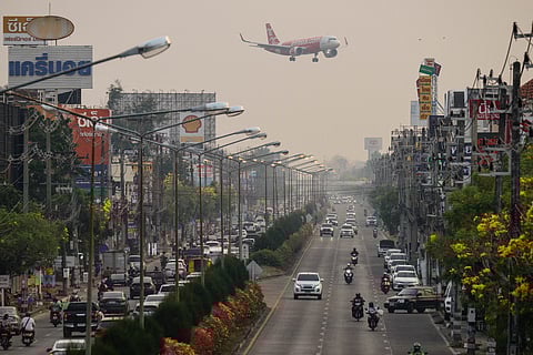 A passenger plane prepares to land at the airport as commuters drive on the road below on a heavily polluted day in Chiang Mai on April 2, 2026.