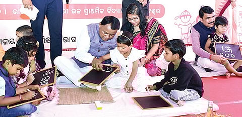 Chief Minister Mohan Charan Majhi teaching a girl child to write Odia alphabets on a slate, at a Khadi Chhuan programme in Bhubaneswar