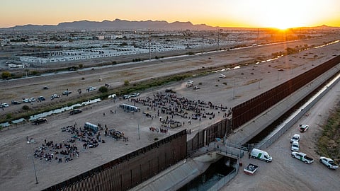 As the sun sets, migrants wait outside a gate in the border fence to enter El Paso, Texas, to be processed by Border Patrol, May 11, 2023.