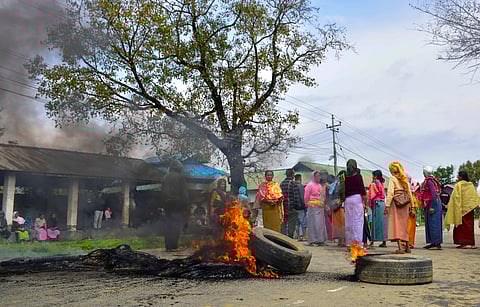 People set fire to tyres as they block a road in protest after two children were killed and their mother was injured in a bomb attack, in Bishnupur district, Manipur, Tuesday, April 7, 2026.