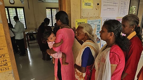 Voters, including women and a young mother carrying her child, wait in a queue to cast their ballots at the Government ITI Varkala during the Kerala Assembly Election on Thursday.
