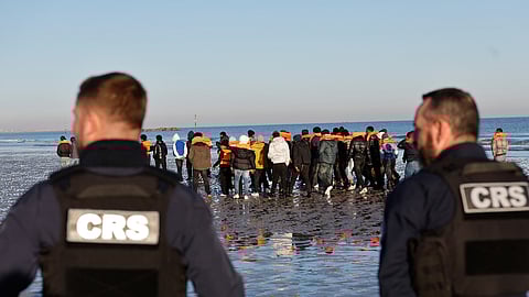 Policemen look at migrants as they board a small boat in an attempt to reach Britain on Wednesday, April 8, 2026, in Malo-les-Bains, northern France.