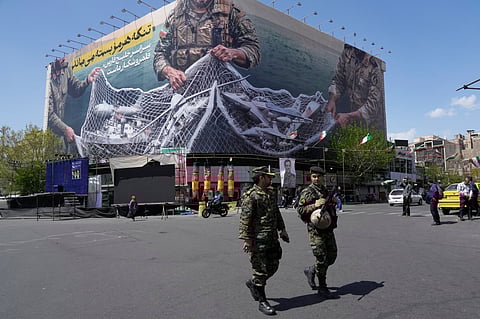 Two police officers walk in front of an anti-U.S. billboard depicting American aircraft being caught by Iranian armed forces in a fishing net beneath the words in Farsi, "The Strait of Hormuz will remain closed, The entire Persian Gulf is our hunting ground," in Tehran, Iran, Sunday, April 5, 2026.
