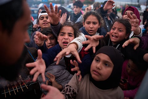 Displaced families extend their hands while waiting for donated food beside the tents they use as shelters after fleeing Israeli bombardment in southern Lebanon, in Beirut, Lebanon, Thursday, April 9, 2026.
