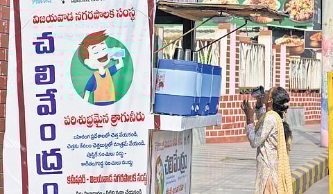 A woman quenches her thirst as she drinks water from a kiosk setup by VMC on a sunny afternoon in Vijayawada.